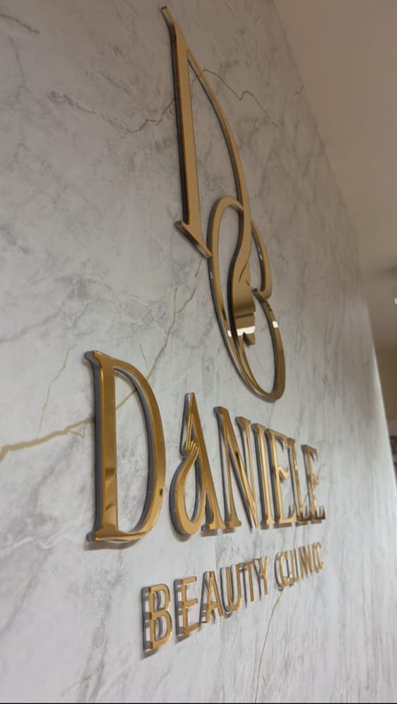 Letreiro dourado Daniele Beauty Clinic aplicado sobre parede de mármore